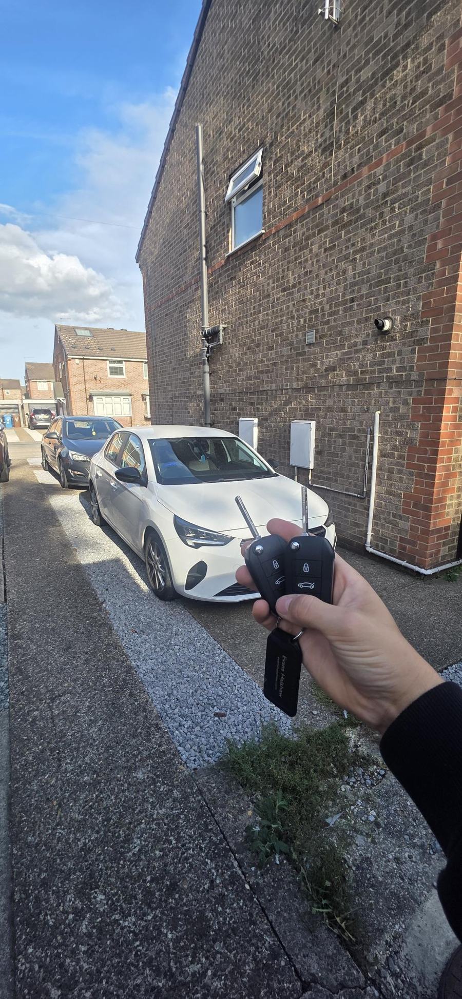 Two Vauxhall Corsa keys with blades out, in front of a white Corsa