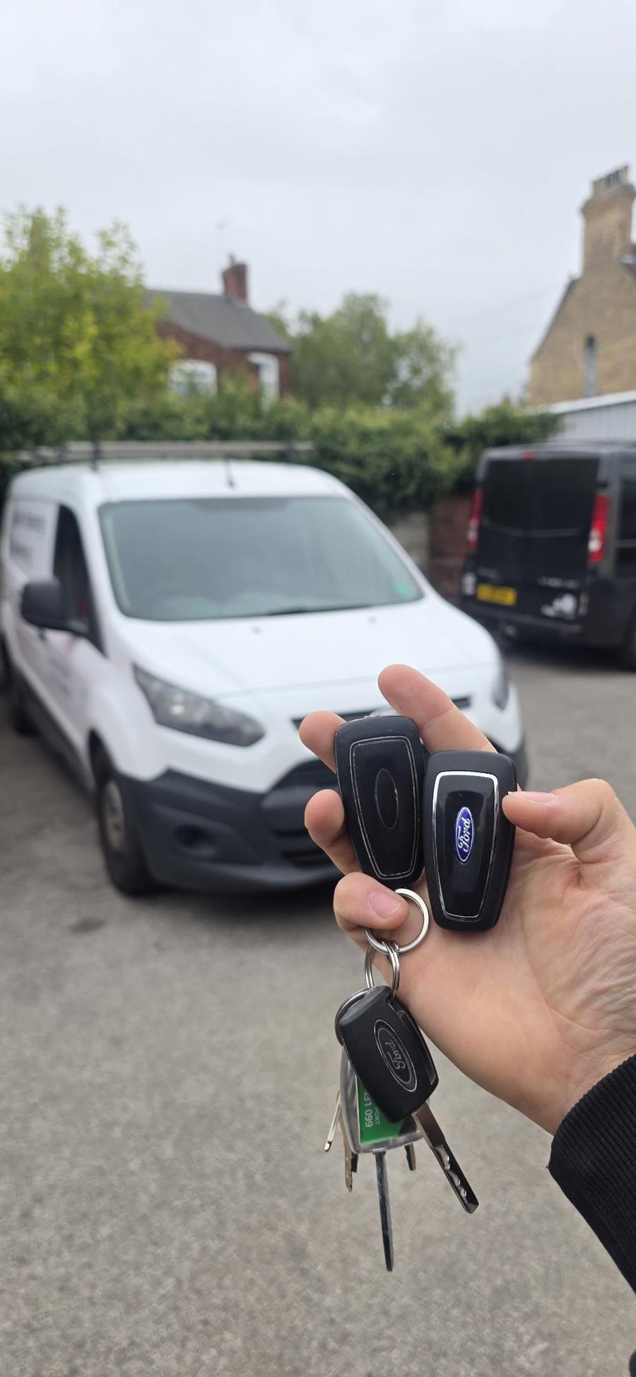 Ford Transit keys and fobs held in front of a white Ford van