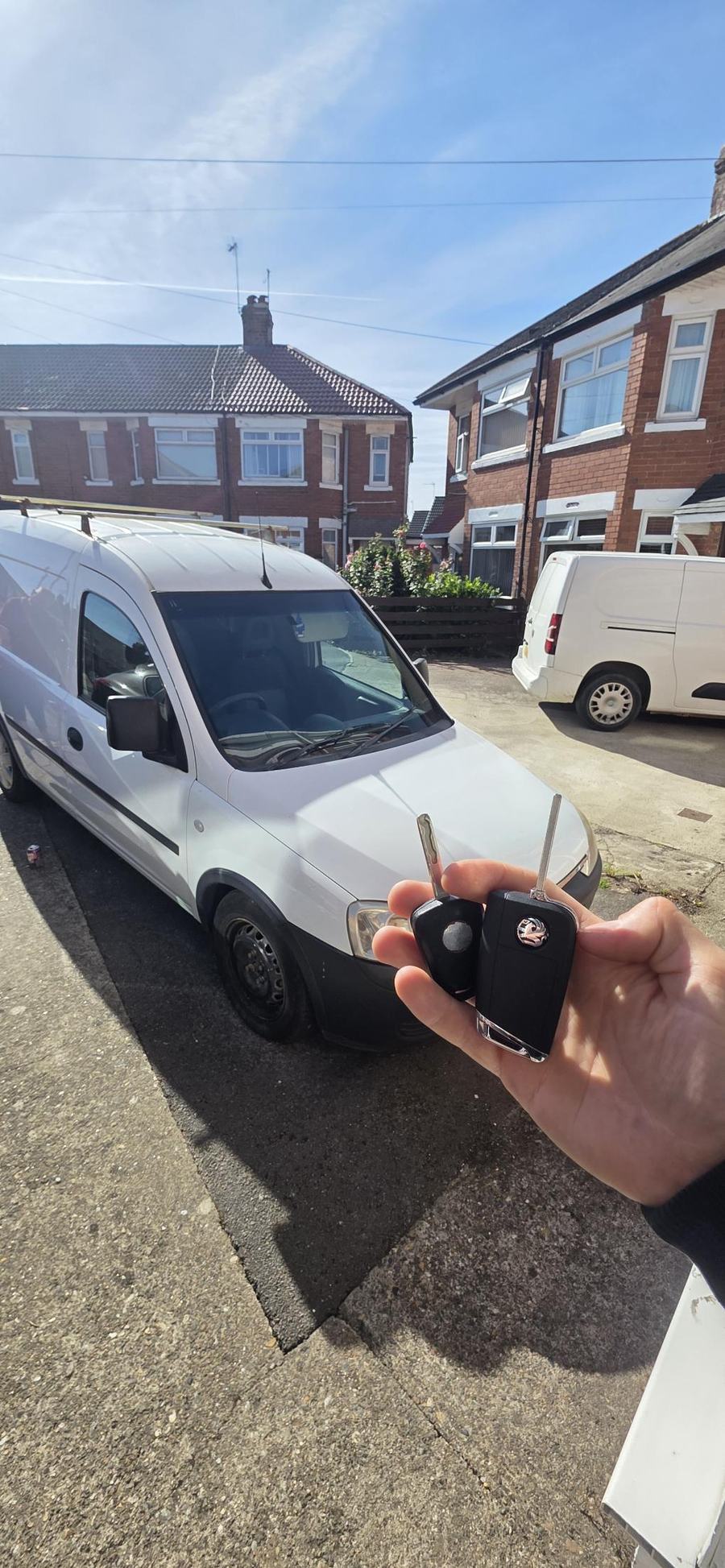 Two Vauxhall keys held in front of a white van on a residential street